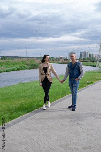 lovely happy couple walking in park by the river holding hands. brunette woman and bald man. wife and husband. successful marriage  true love. romantic walk on a date