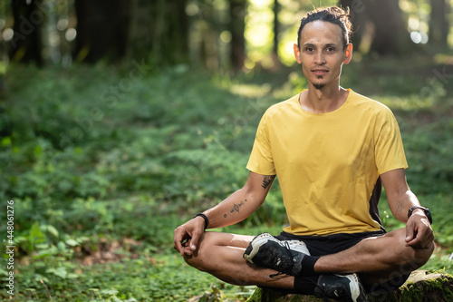 Junger Mann mit dunkler Haut sitzt im Wald und meditiert auf Baumstamm
