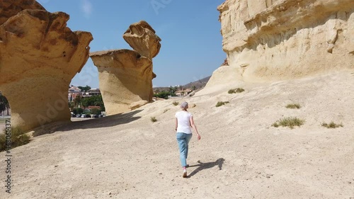 A steady shot of Girl walking through the desert near yellow futuristic rock.