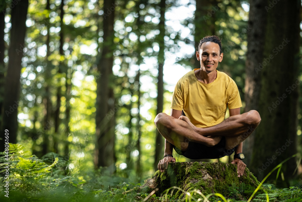 Obraz premium Junger Mann mit dunkler Haut im Lotussitz beim Yoga im Wald in der Natur