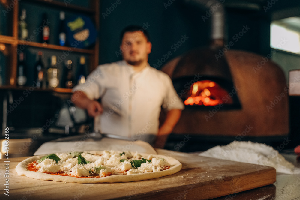 The chef prepares pizza in a wood-fired oven. Cooking pizza. The cook puts the pizza in the oven.