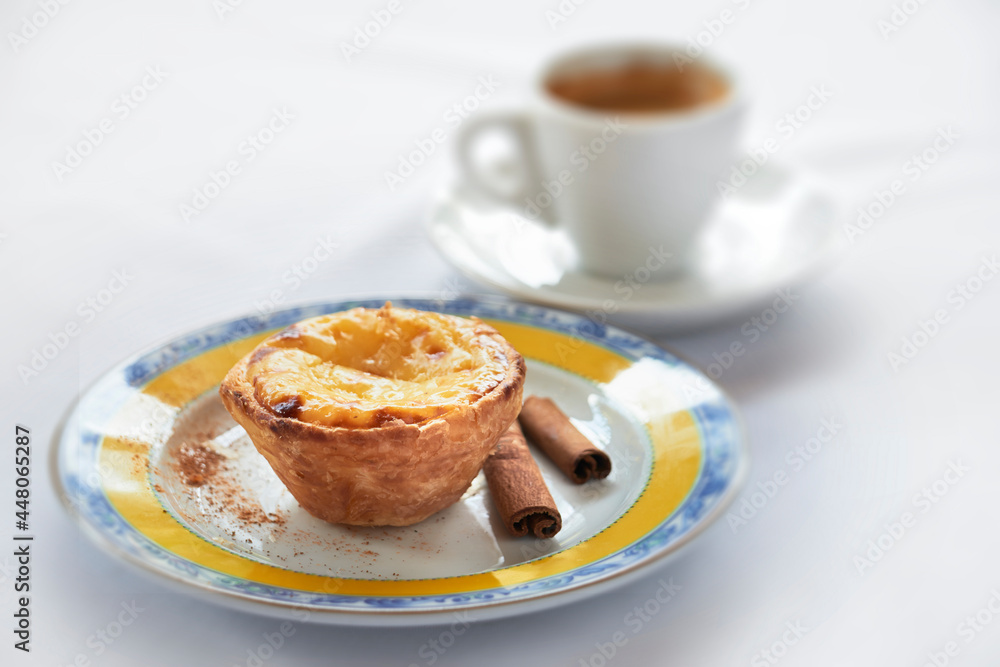Pastel de Belem em primeiro plano com xícara de café desfocada ao fundo