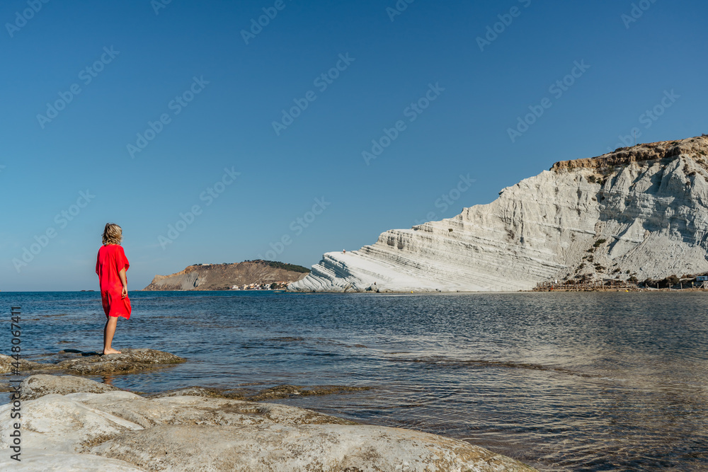 Scala dei Turchi,Sicily,Italy.Happy woman in red dress standing on beach, enjoying sunny summer day.View of white rocky cliffs,turquoise clear water.Travel holiday scenery.Girl on vacation Scala dei Turchi,Sicily,Italy.Happy woman in red dress standing on beach, enjoying sunny summer day.View of white rocky cliffs,turquoise clear water.Travel holiday scenery.Girl on vacation