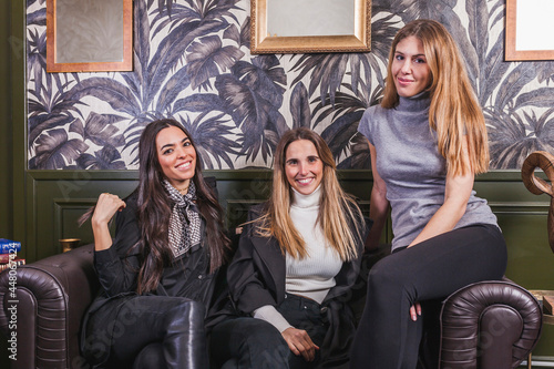 Foto Three happy beautiful girls sitting on sofa at restaurant