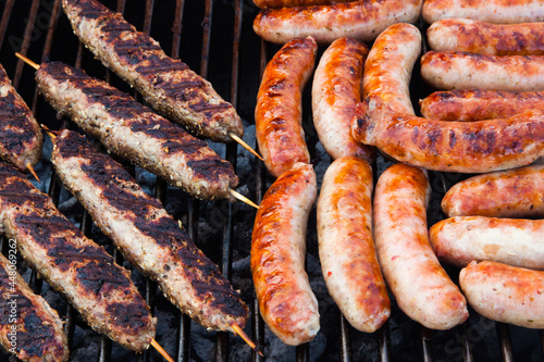 Sausages and minced meat on wooden sticks are cooked on the grill.