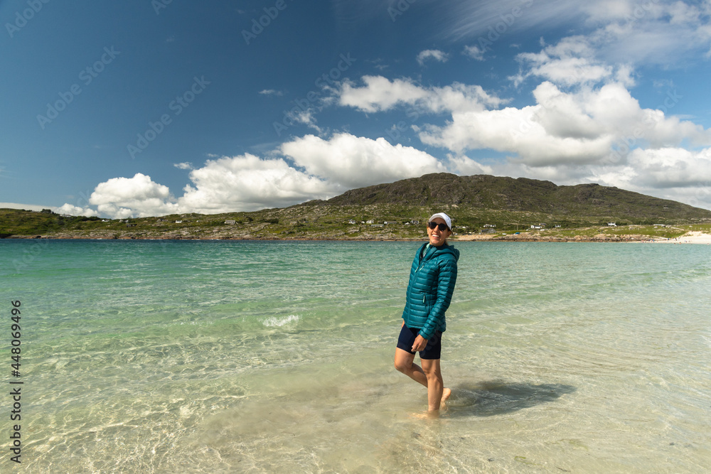 Traveler woman walking and smiling along white sand beach and clear water at Dog's Bay Galway Ireland Traveler woman walking and smiling along white sand beach and clear water at Dog's Bay Galway Ireland