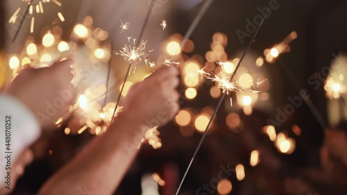 Close up hands holding sparklers group of friends celebrating waving sparkler fireworks dancing enjoying new years eve party having fun holiday celebration at evening. Bengal Flicker Blurred Bokeh.