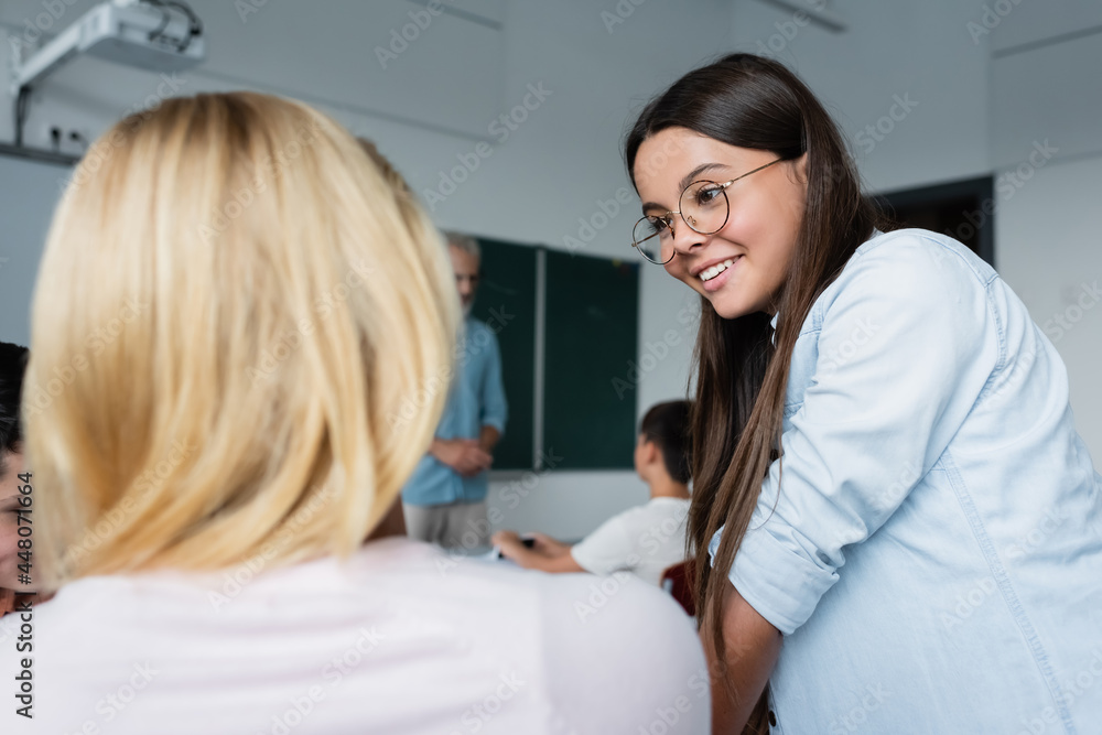 Fototapeta premium Positive schoolgirl looking at blurred friend