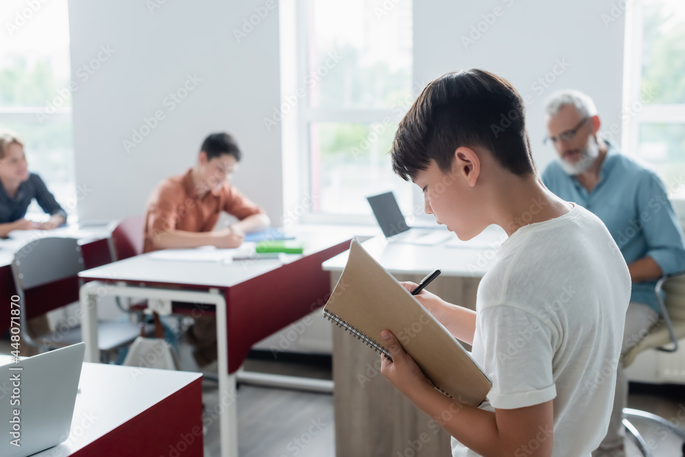 Asian schoolboy with notebook standing in classroom Asian schoolboy with notebook standing in classroom