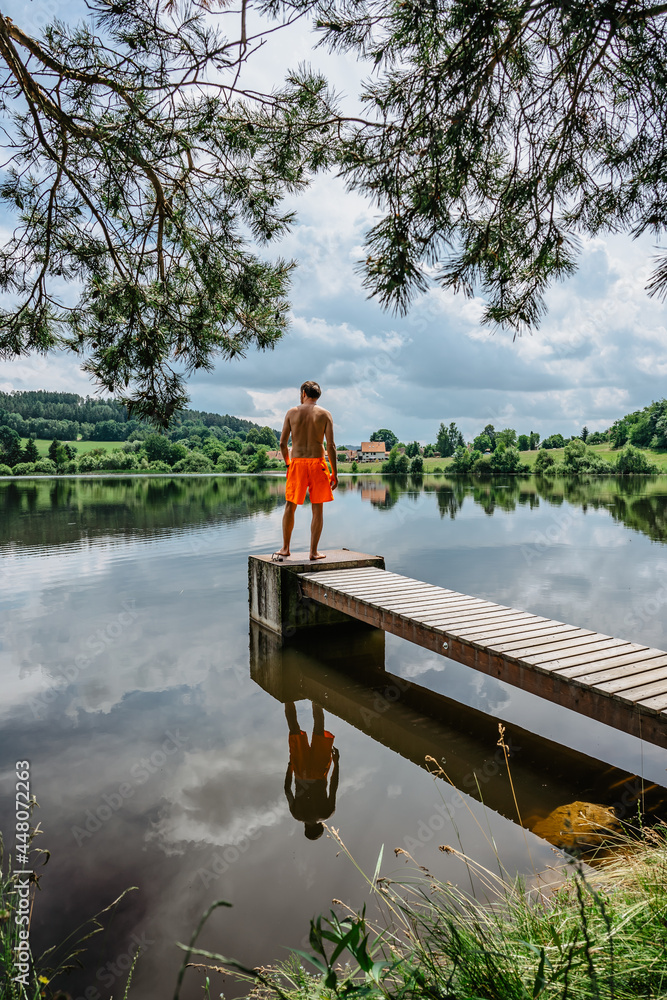 Rear view of man jumping from wooden pier with joy in to the water,nature reflected in lake.Having summer fun by pond.Travel vacation, youth holiday concept.Happy active lifestyle, entertaintment Rear view of man jumping from wooden pier with joy in to the water,nature reflected in lake.Having summer fun by pond.Travel vacation, youth holiday concept.Happy active lifestyle, entertaintment