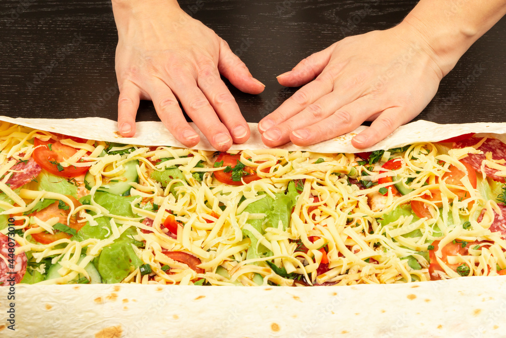 female hands wrap fresh vegetable salad with cheese in pita bread. cooking shawarma on a black wooden table