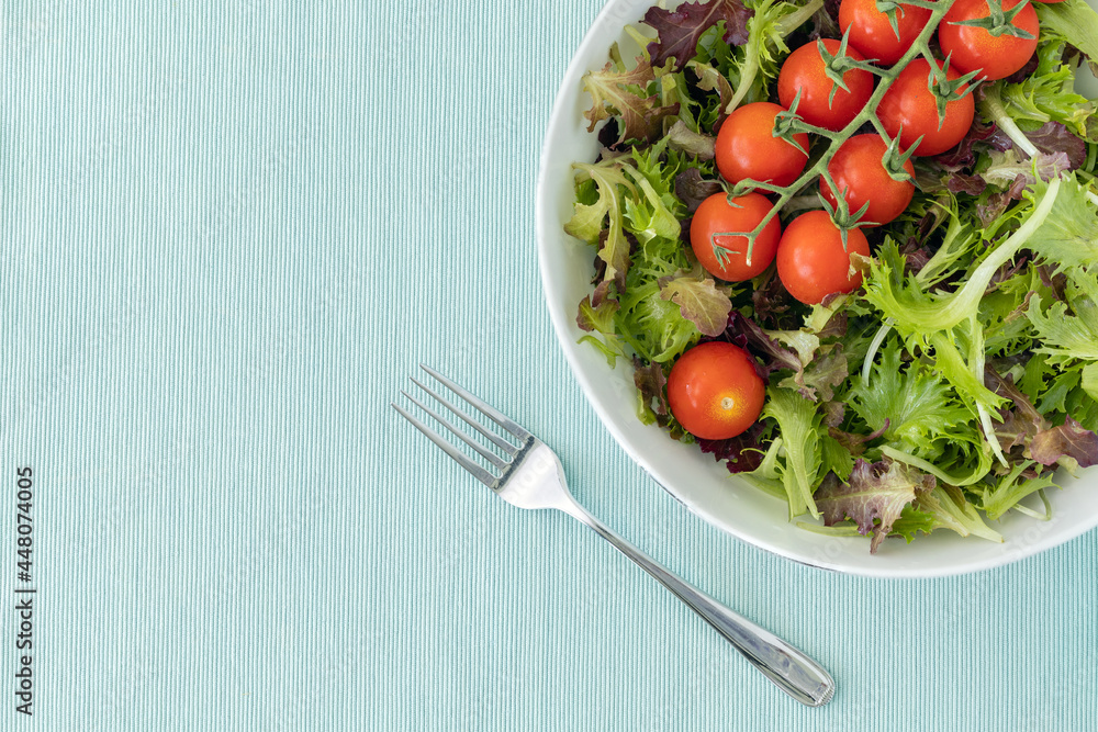 Lettuce leaves and cherry tomatoes in a bowl and a fork on light blue surface, top view with copy space Lettuce leaves and cherry tomatoes in a bowl and a fork on light blue surface, top view with copy space