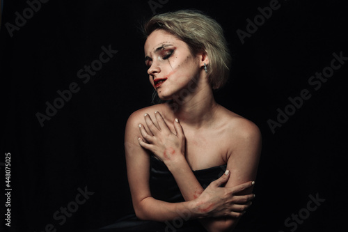 Portrait of a girl on a black background. A girl with smeared makeup hugs herself.