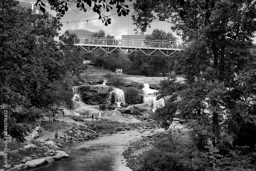 Black and white photo of waterfall and steel suspension bridge in park