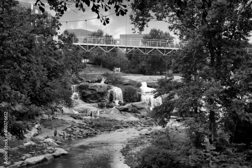Black and white photo of waterfall and steel suspension bridge in park