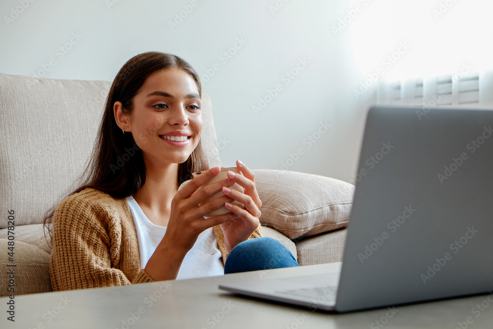 Young beautiful woman sitting alone at home and enjoying alone time with her laptop. Portrait of female sitting on the floor and watching shows on a streaming service. Close up, copy space, background Young beautiful woman sitting alone at home and enjoying alone time with her laptop. Portrait of female sitting on the floor and watching shows on a streaming service. Close up, copy space, background