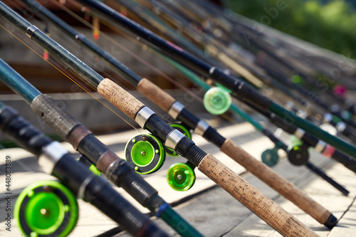 Many fishing rods on the wooden pier by the river or lake on a sunny day