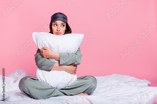 Photo of shiny adorable young woman nightwear sitting duvet hugging pillow looking empty space isolated pink color background