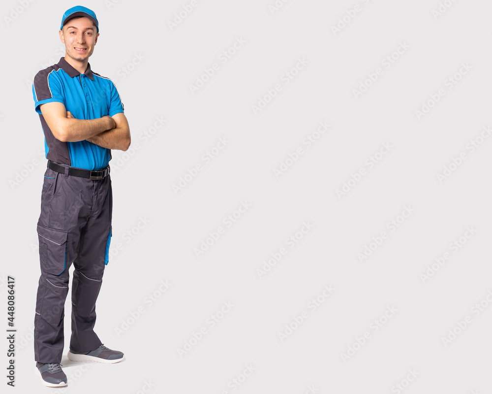 The full-length photo of a delivery man in grey-blue uniform folded his arms on the chest looking at the camera. The full-length photo of a delivery man in grey-blue uniform folded his arms on the chest looking at the camera.