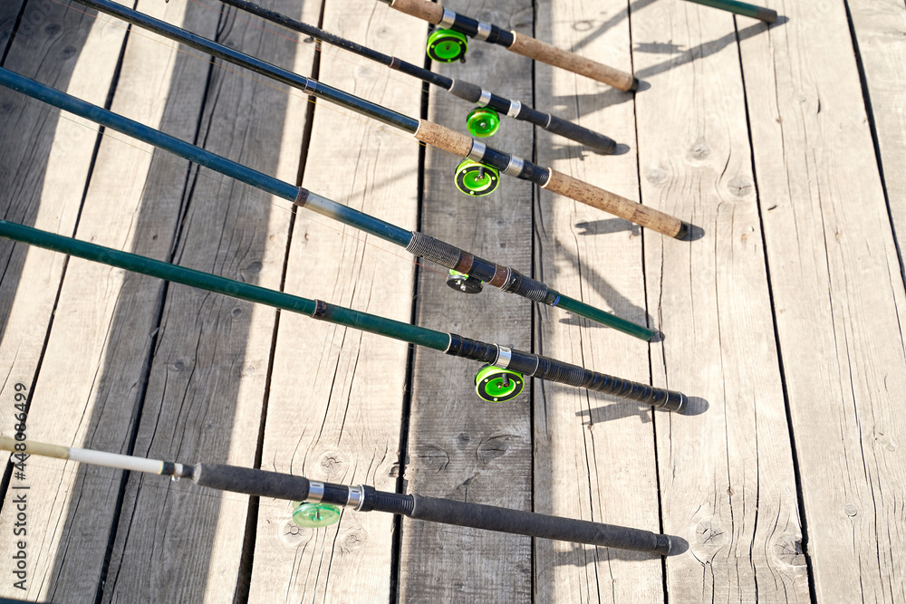 Many fishing rods on the wooden pier by the river or lake on a sunny day