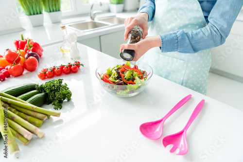 Cropped top view woman in apron adding spices to salad in the kitchen