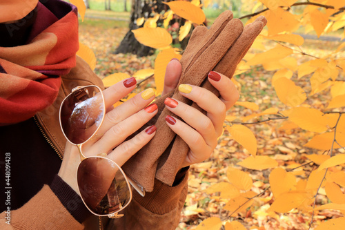 A girl with an autumn manicure holds accessories in her hands.