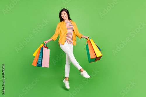 Photo of adorable pretty young woman dressed casual clothes holding shopping bags walking isolated green color background