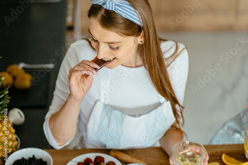 View from above happy cheerful young woman try fruit marshmallow while preparing berry pastille  dish with fresh fruits in home kitchen. Healthy food  homemade sweets  preparations cook concept.