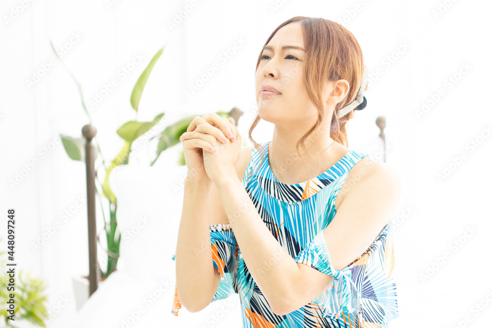 明るい部屋の窓際で、お願いのジェスチャーをする、ワンピースを着た若い女性