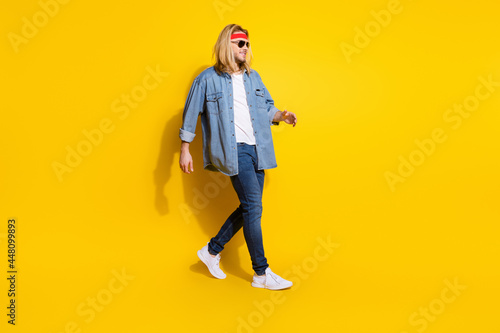 Photo of cool funky young guy dressed denim shirt smiling walking empty space isolated yellow color background