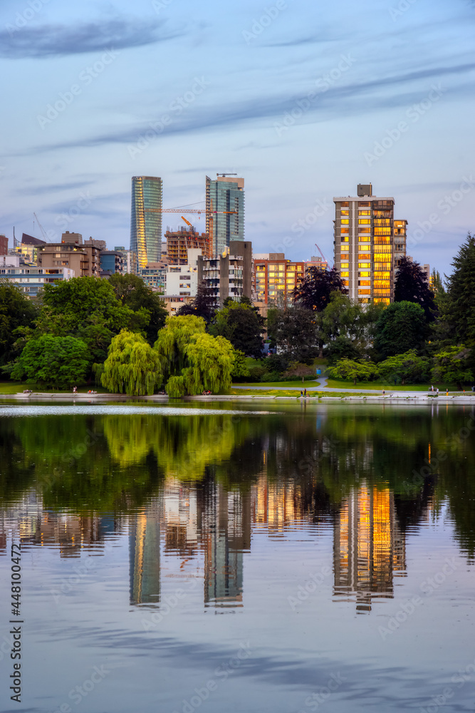 View of Lost Lagoon in famous Stanley Park in a modern city with buildings skyline in background. Colorful Sunset Sky. Downtown Vancouver, British Columbia, Canada.