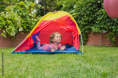 The little girl is playing and having fun in the shade of the tent in the garden of their house.