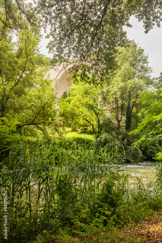 The ruins of the Roman arch bridge of Augustus  in Narni  Terni  Umbria. The remains of the bridge over the Nera river. The big and ancient stone arch  against the blue sky. Trees and dense vegetation