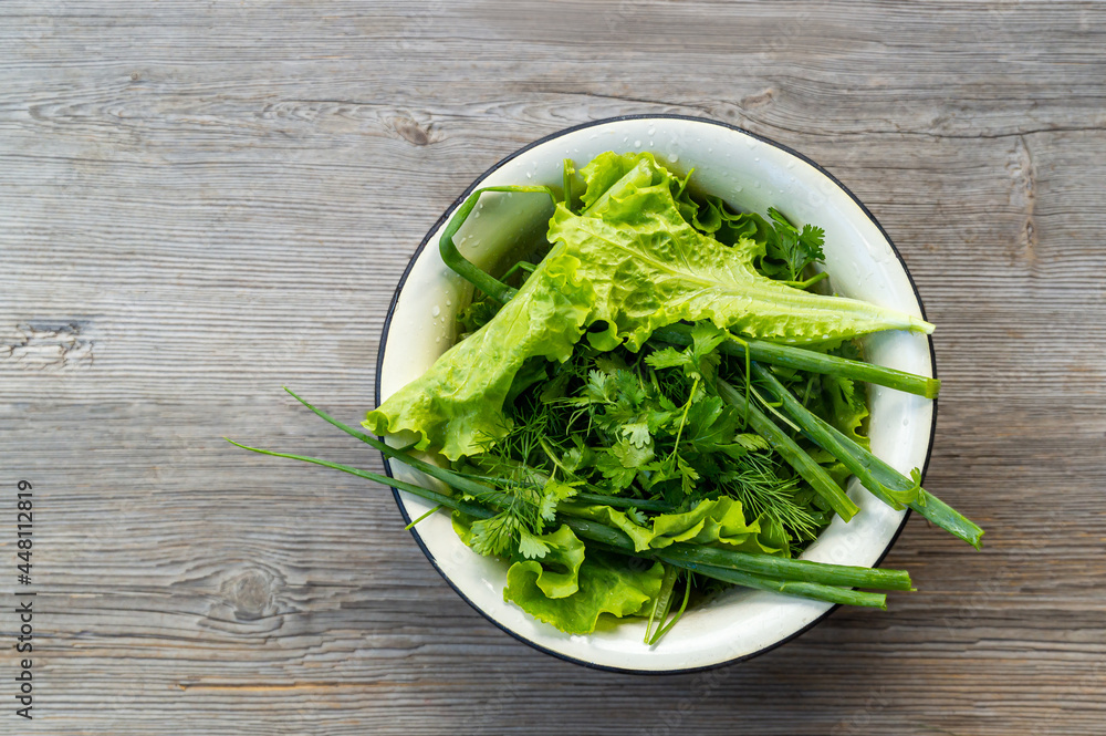 fresh herbs for salad. green onions, parsley, dill and lettuce in a bowl on a gray wooden background fresh herbs for salad. green onions, parsley, dill and lettuce in a bowl on a gray wooden background