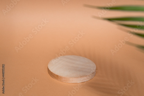 Round wooden podium for food products or cosmetics on a bright brown background with palm tree leaves shadows