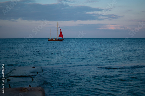 Evening sea skyline with distant ship sailing under red sail