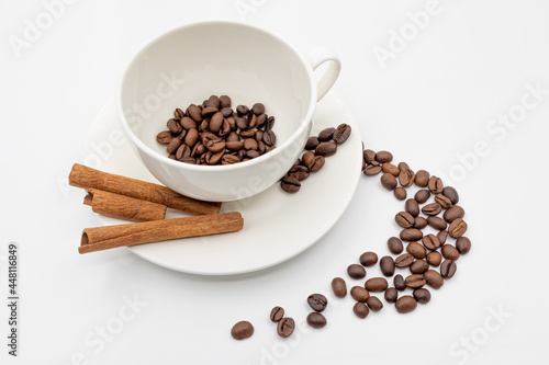 Coffee beans in a cup and cinnamon sticks on a white saucer