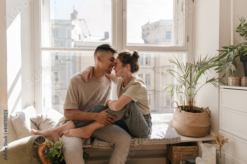 Fotografie Cute young couple sitting on windowsill against city view background
