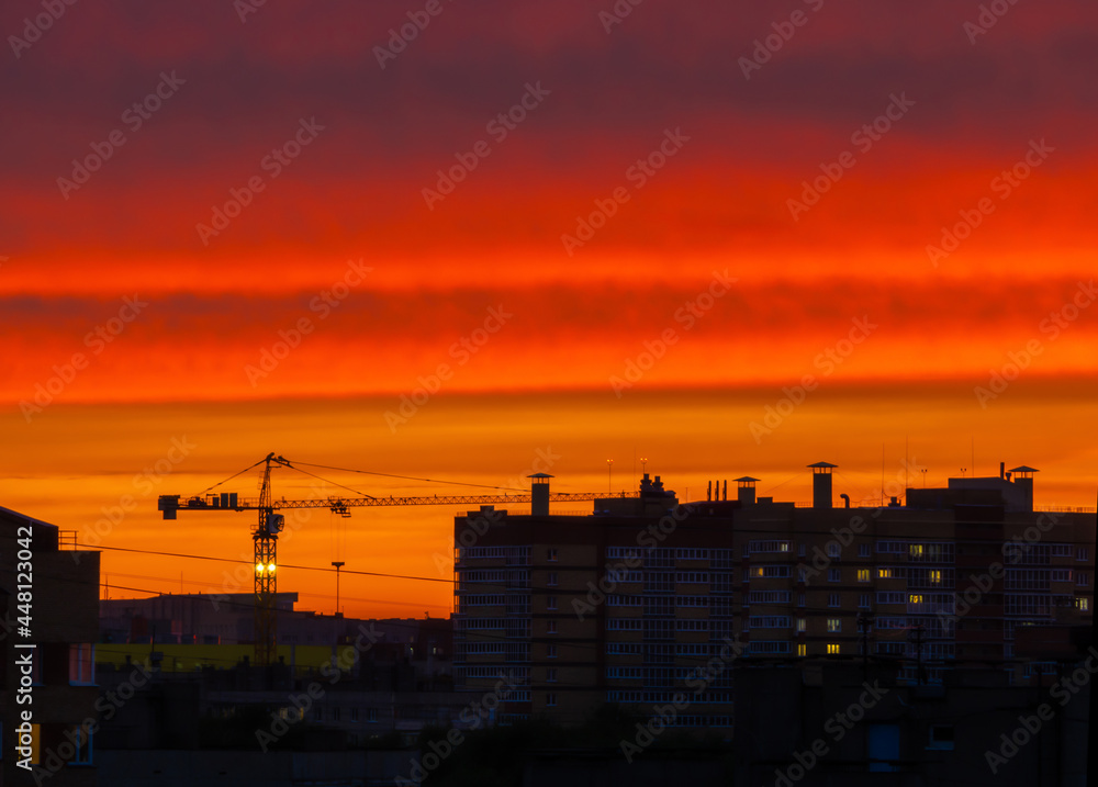 Urban profile with roofs of houses and a construction crane on the background of the sunset sky. Place for your text..Fantastic sunset with bright red sky over the city. Urban profile with roofs of houses and a construction crane on the background of the sunset sky. Place for your text..Fantastic sunset with bright red sky over the city.