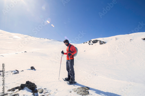 A man standing in the mountain full of snow. holding hiking sticks. Winter trip. Red jacket
