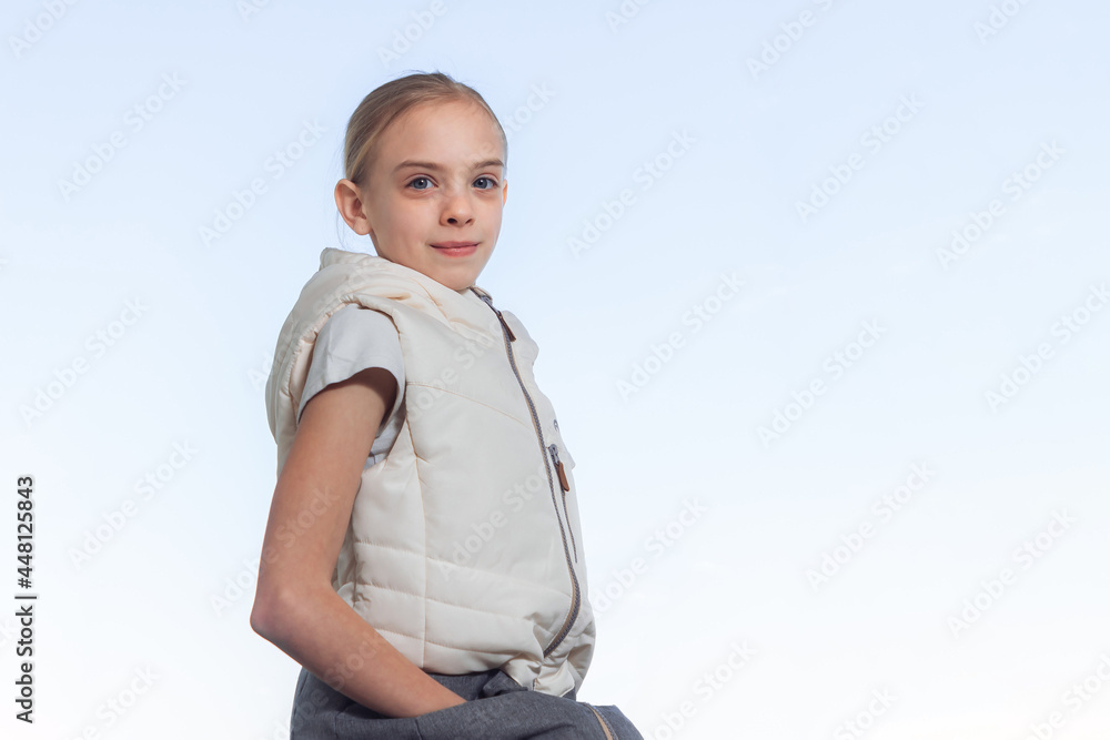 A blonde pretty attractive girl in a jacket is sitting on a sunny spring day outdoors against the background of a bright blue sky. A blonde pretty attractive girl in a jacket is sitting on a sunny spring day outdoors against the background of a bright blue sky.