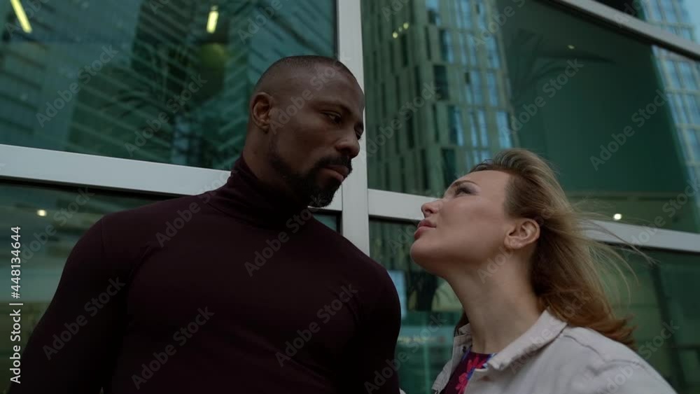 a bearded African-American man and a blonde woman stand against a glass wall with a reflection of a high-rise building and look at each other. the camera is moving a bearded African-American man and a blonde woman stand against a glass wall with a reflection of a high-rise building and look at each other. the camera is moving