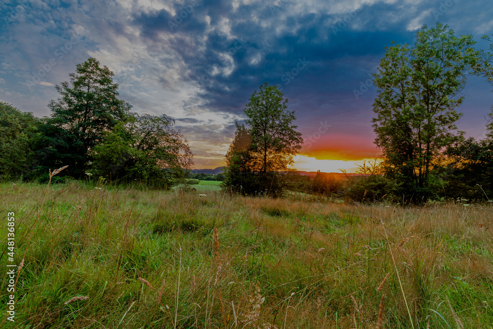 Colorful sunset on a warm summer evening over the rolling hills in Limburg. The sky showed amazing colours which gives a natural contrast to the green colours of the  forest and meadow