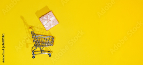 Creative concept with shopping trolley with gifts on a yellow background. Copy space