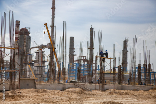 Construction of modern asphaltic bitumen plant. Assembling building columns. Workers on forms and concrete pump hose. Focus on worker.