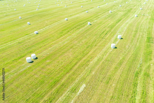 Aerial view agricultural landscape. Straw packages on field. Flying over cereal bale of hay wrapped in plastic white foil. Agricultural background. Close-up of bales of rolled hay. Haymaking photo