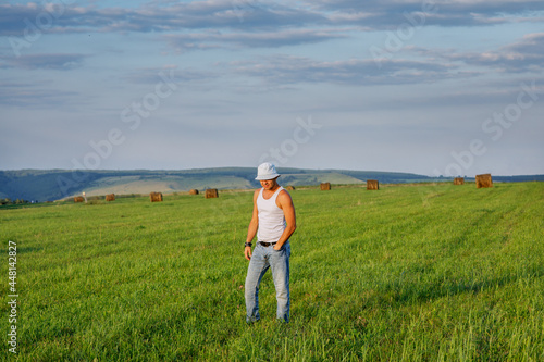 A farmer in jeans walks through the field among bales of hay. Harvest. Beautiful summer landscape on the farm. 