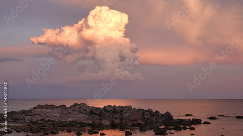 Huge masses of clouds hanging in red and white and crimson hues in the sky and crimson cliffs and pebbles on the beach