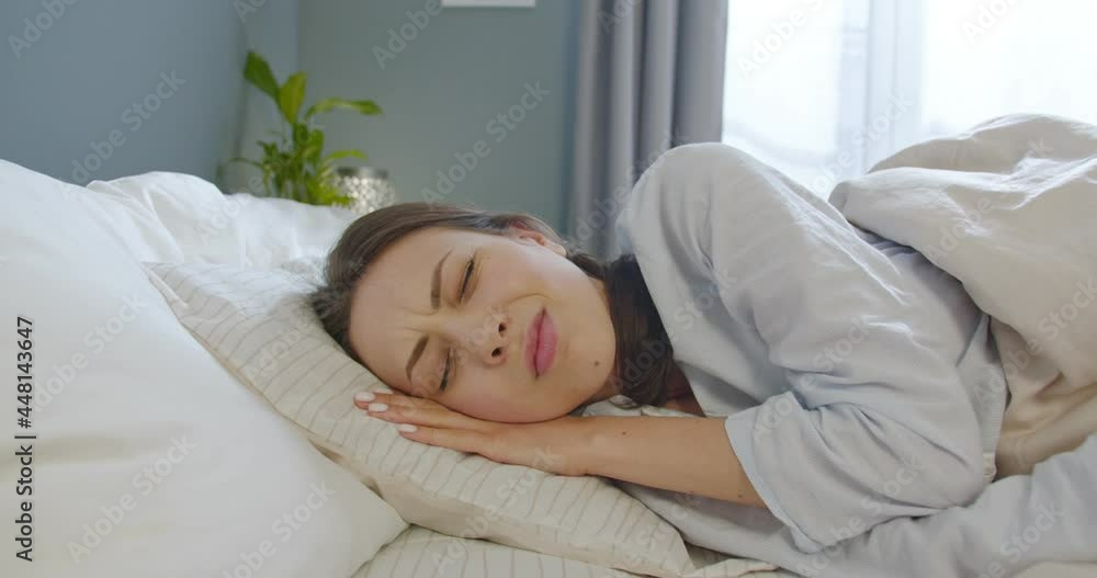 Close up of Caucasian beautiful young woman sleeping in bed in bedroom and waking up from noise in bad mood Unhappy female trying to sleep annoyed by bad noisy room neighbors covering ears with pillow