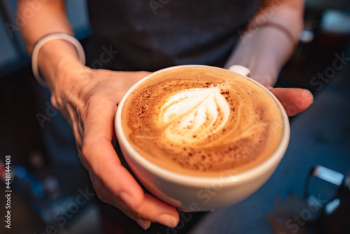 Barista holds a cup with just made cappuccino coffee with beautiful milk foam
